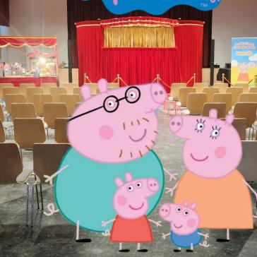 Ein Saal mit Stuhlreihen vor einer roten Puppenbühne. Peppa Wutz und Familie sind digital eingefügt. Schrift: „Puppentheater live“.