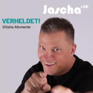 Ein Mann mit kurzem Haar und schwarzem Shirt lacht und zeigt mit beiden Händen auf die Kamera. Oben steht „Jascha LIVE“, darunter „VERHELDET! H(aha)-Momente“ auf grauem Hintergrund.