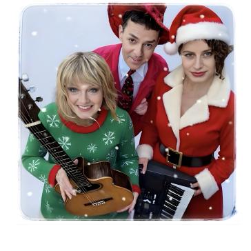 Drei lächelnde Personen in weihnachtlicher Kleidung: Eine Frau mit Gitarre in grünem Schneeflocken-Pullover, ein Mann im roten Anzug mit Weihnachtsmann-Mütze, eine Frau im roten Santa-Kostüm mit Keyboard.