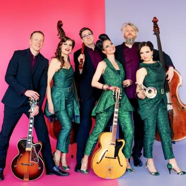 Sechsköpfige Band in grünen und dunklen Outfits, posierend mit E-Gitarren, Kontrabass, Trompete und Gitarren vor pink-lila Hintergrund.