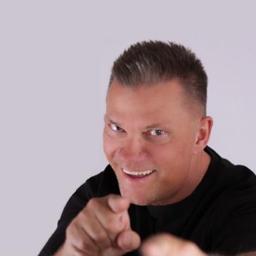 Ein Mann mit kurzem Haar und schwarzem Shirt lacht und zeigt mit beiden Händen auf die Kamera. Oben steht „Jascha LIVE“, darunter „VERHELDET! H(aha)-Momente“ auf grauem Hintergrund.