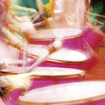 Verwackelte Aufnahme einer Person am pinken Schlagzeug, Drumsticks in Bewegung, farbig verwischter Hintergrund – dynamische Live-Szene.