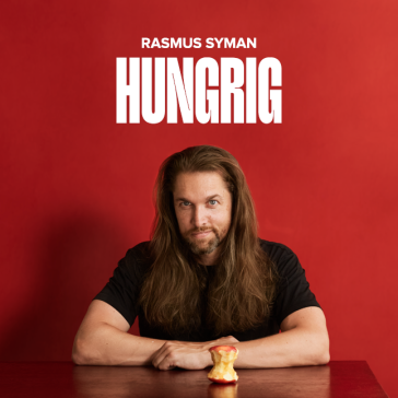 Bärtiger Mann mit langen braunen Haaren in schwarzem T-Shirt am Tisch, halb gegessener Apfel davor, rote Wand, weißer Schriftzug ‚RASMUS SYMAN – HUNGRIG'.