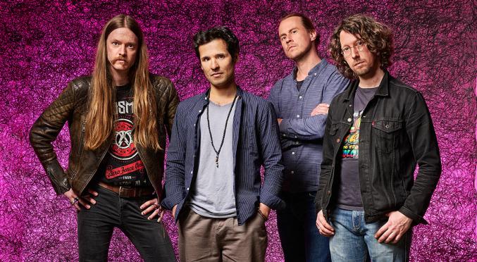 Band-Porträt vor einem leuchtend pinken Hintergrund: vier Mitglieder, lässige Outfits, teils Lederjacke, entspannte Posen mit individueller Ausstrahlung.