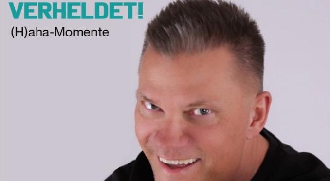 Ein Mann mit kurzem Haar und schwarzem Shirt lacht und zeigt mit beiden Händen auf die Kamera. Oben steht „Jascha LIVE“, darunter „VERHELDET! H(aha)-Momente“ auf grauem Hintergrund.
