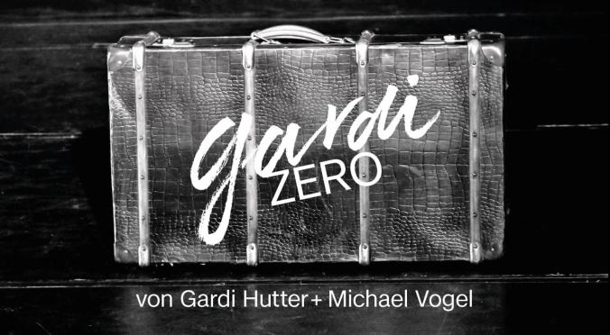 Ein alter Koffer mit Lederstruktur steht auf einer dunklen Bühne. Darauf steht in weißer Schrift „gardi ZERO“. Unten steht: „von Gardi Hutter + Michael Vogel“.