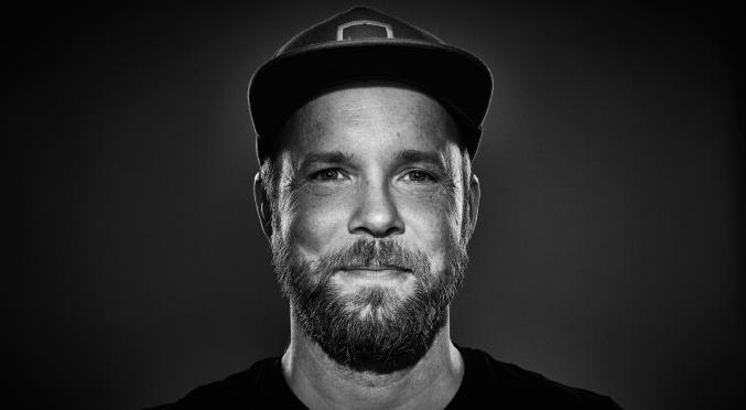 Porträt eines Mannes mit Basecap, Vollbart und ernstem Blick, fotografiert in Schwarz-Weiß mit dramatischer Beleuchtung.