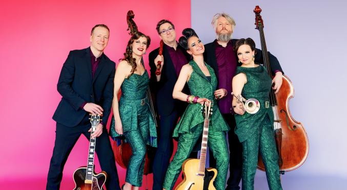 Sechsköpfige Band in grünen und dunklen Outfits, posierend mit E-Gitarren, Kontrabass, Trompete und Gitarren vor pink-lila Hintergrund.