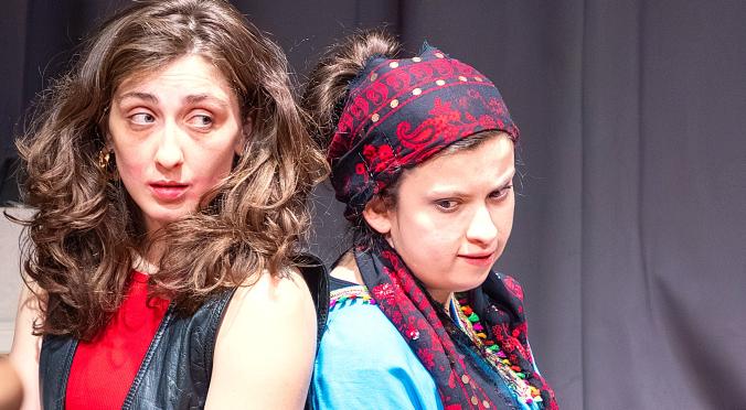 Zwei Frauen vor dunklem Hintergrund: Links mit lockigem Haar, roter Bluse und schwarzer Weste, rechts mit rot-schwarzem Tuch und blauem Oberteil.