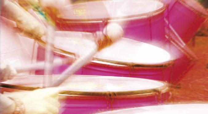 Verwackelte Aufnahme einer Person am pinken Schlagzeug, Drumsticks in Bewegung, farbig verwischter Hintergrund – dynamische Live-Szene.