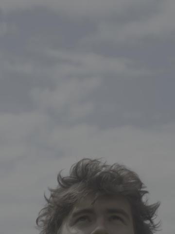 Porträt eines Menschen mit nassen Haaren, das nur die obere Gesichtshälfte zeigt. Der Hintergrund ist ein großer, grauer Himmel.