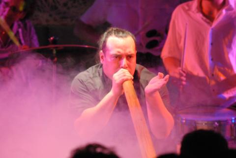 Ein Mann spielt Didgeridoo auf einer Bühne. Um ihn herum ist Nebel.