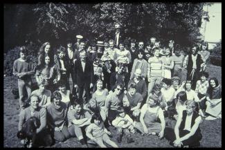 Gruppenbild mit ca. 50 Personen, Kindern, jungen und alten Erwachsenen, die auf einer Wiese sitzen und stehen.